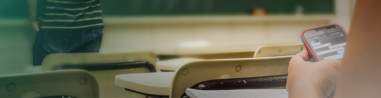 Student playing on phone while a teacher is writing on a blackboard.